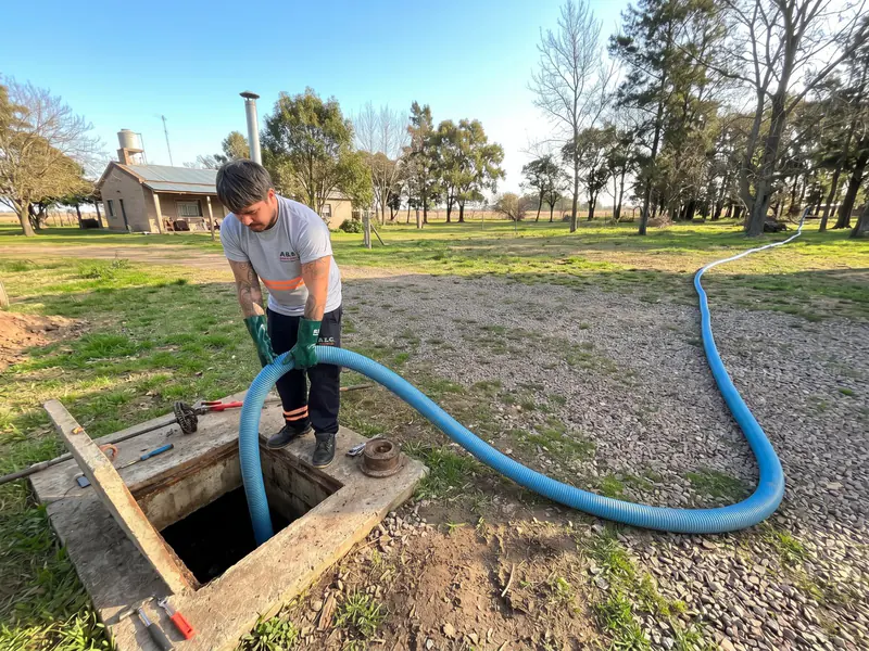 Operario acomodando una manguera azul en una cámara abierta, en el terreno de una casa de campo